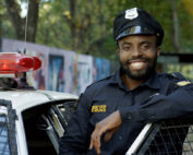 A smiling police officer stands next to his cruiser.