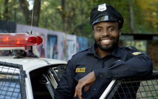 A smiling police officer stands next to his cruiser.
