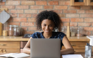 A smiling adult online student uses her laptop to consult with her academic advisor