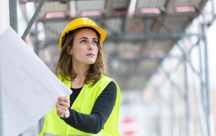 A female architect examines building plans while onsite at a construction project