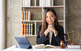 A female lawyer working with a laptop and legal books. A gavel and the scales of justice sit beside her on a desk.