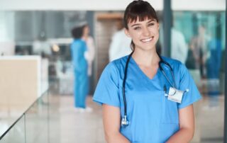 A female nurse in scrubs smiles broadly at the camera.