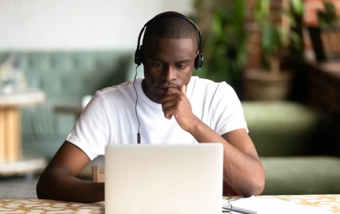 An African American college student wearing headphones focuses a video lecture on his laptop.